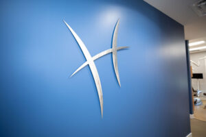 Modern dental office logo mounted on a blue wall with a glimpse of the treatment area in the background.